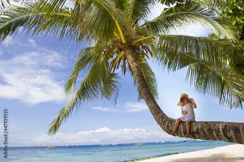 Photo: young happy child girl in summer hat on tropical sea background young happy child girl in summer hat on tropical sea background