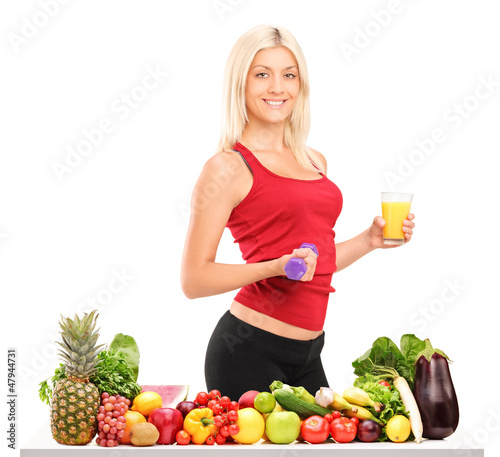 Photo: Female athlete holding a dumbbell and glass of juice behind a ta Female athlete holding a dumbbell and glass of juice behind a ta
