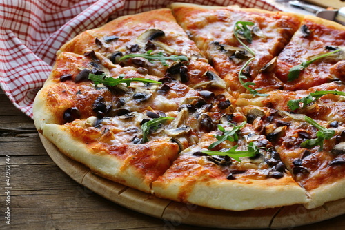 Photo: Italian pizza with mushrooms and olives on a wooden board Italian pizza with mushrooms and olives on a wooden board