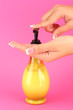 woman squeezing lotion on her hand, on pink background close-up