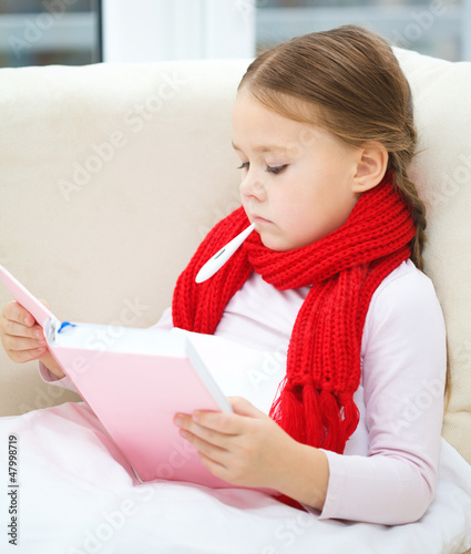 Photo: Ill little girl with thermometer is reading book Ill little girl with thermometer is reading book