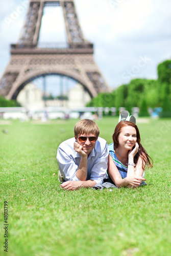 Photo: Closeup of happy positive couple laying on the grass near the Ei Closeup of happy positive couple laying on the grass near the Ei