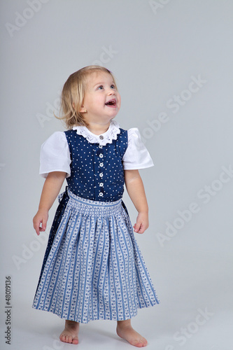 Photo: Kind im Dirndl blickt auf ihren Text lachend Kind im Dirndl blickt auf ihren Text lachend