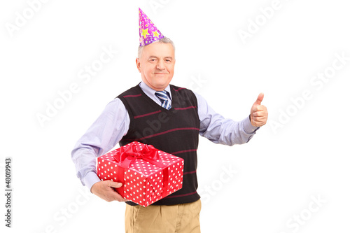 Photo: A gentleman with party hat holding a gift and giving a thumb up A gentleman with party hat holding a gift and giving a thumb up