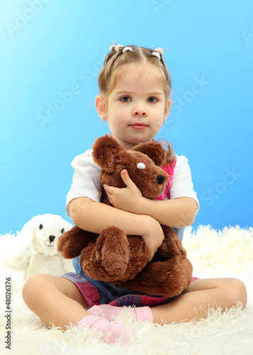Photo: cute little girl playing with toy bear, on blue background cute little girl playing with toy bear, on blue background