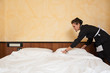 Photo: Chambermaid woman changing sheets in a hotel room. Chambermaid woman changing sheets in a hotel room.