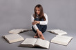 Photo: Young girl studying surrounded by books against grey background. Young girl studying surrounded by books against grey background.