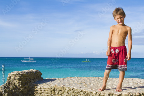 Photo: young happy child boy on rocks on tropical sea background young happy child boy on rocks on tropical sea background