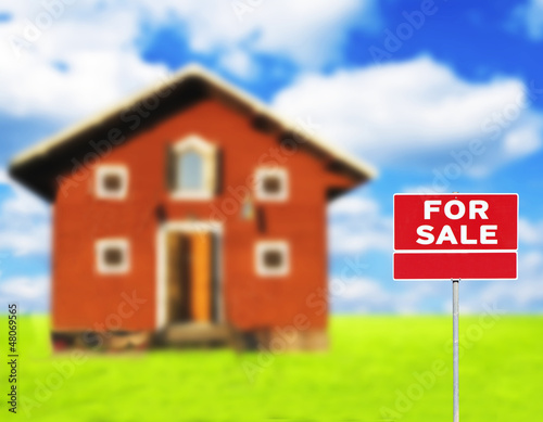 Photo: "FOR SALE" sign against wooden house on beautiful meadow in back "FOR SALE" sign against wooden house on beautiful meadow in back