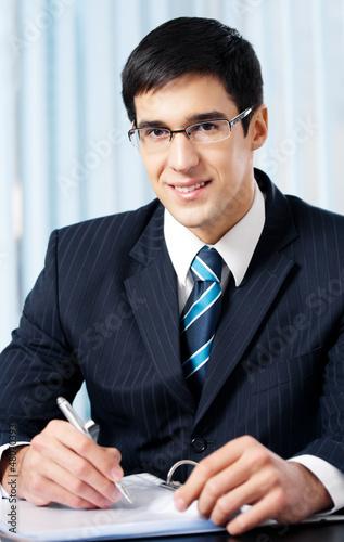 Photo: Portrait of writing smiling businessman working at office Portrait of writing smiling businessman working at office