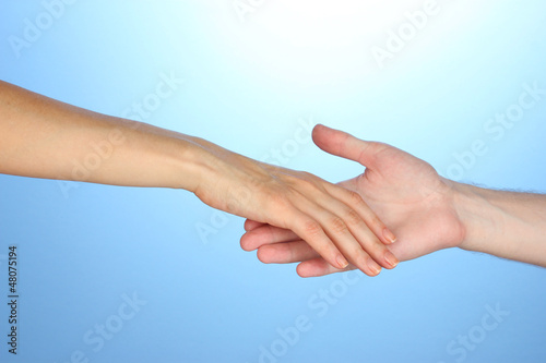 Photo: Women's hand goes to the man's hand on blue background Women's hand goes to the man's hand on blue background