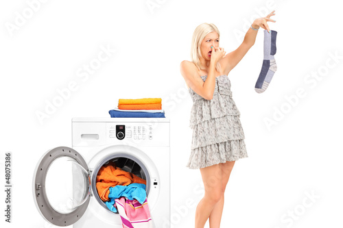 Photo: A housewife holding a male sock and her nose next to a washing m A housewife holding a male sock and her nose next to a washing m