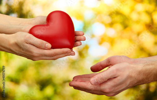Photo: Red heart in woman and man hands, on green background Red heart in woman and man hands, on green background