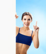 Woman in fitnesswear showing signboard, over blue