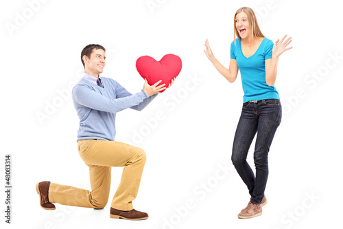 Photo: A smiling male kneeling with red heart and surprised woman A smiling male kneeling with red heart and surprised woman