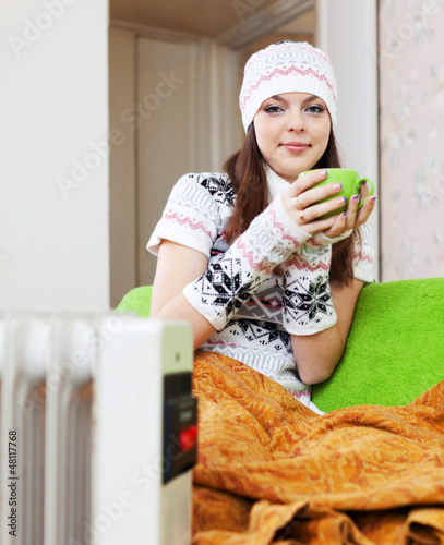 Photo: woman relaxing with cup near heater woman relaxing with cup near heater