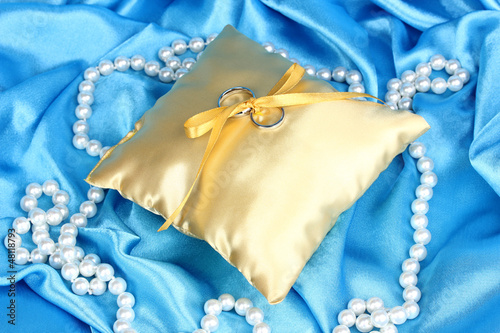Photo: Wedding rings on satin pillow on blue cloth background Wedding rings on satin pillow on blue cloth background