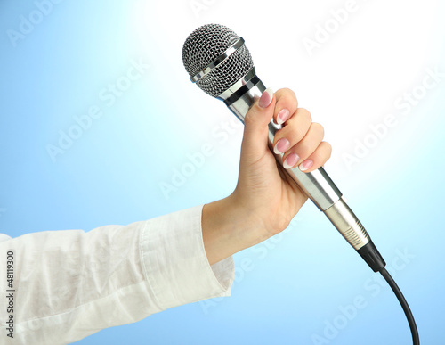 Photo: female hand with microphone, on blue background female hand with microphone, on blue background