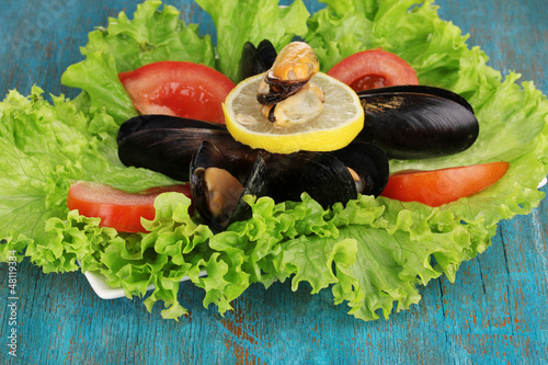 Photo: Snack of mussels and lemon on plate on blue wooden table Snack of mussels and lemon on plate on blue wooden table
