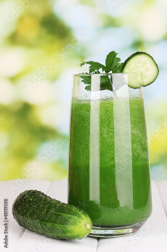 Photo: Glass of cucumber juice on wooden table, on green background Glass of cucumber juice on wooden table, on green background