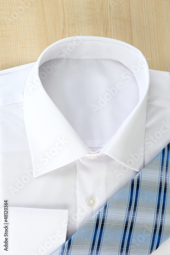 Photo: New white man's shirt with color tie on wooden background New white man's shirt with color tie on wooden background