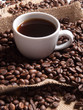 white cup with coffee on burlap background with beans