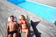 Fancy couple relaxing in longchairs by swimming pool