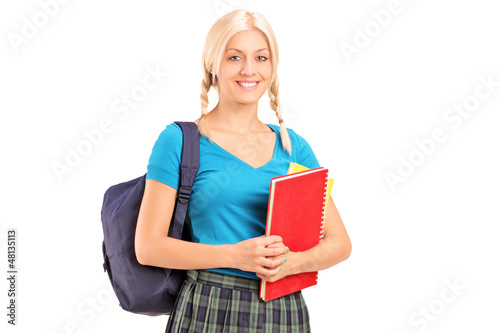 Photo: A female student standing with school bag and holding books A female student standing with school bag and holding books