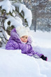 Little girl sits under snow covered branches in the deep snow