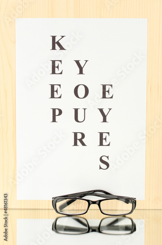 Photo: Eyesight test chart with glasses on wooden background close-up Eyesight test chart with glasses on wooden background close-up