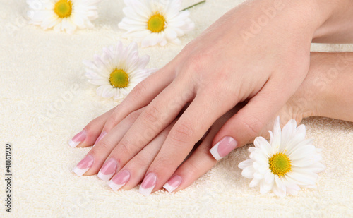 Photo: Woman hands with french manicure and flowers on towel Woman hands with french manicure and flowers on towel