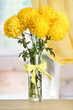 bright yellow chrysanthemums in glass vase, on wooden table