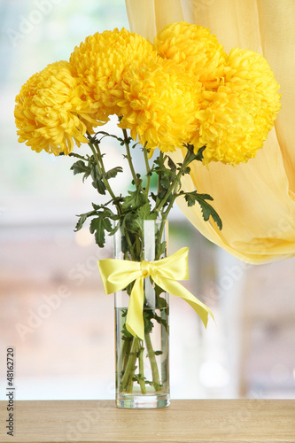 Photo: bright yellow chrysanthemums in glass vase, on wooden table bright yellow chrysanthemums in glass vase, on wooden table