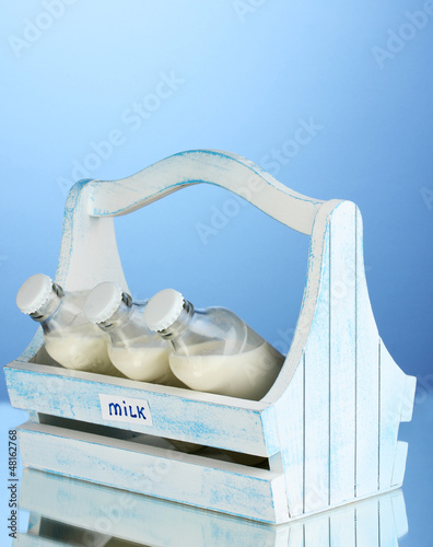 Photo: Milk in bottles in wooden box on blue background Milk in bottles in wooden box on blue background