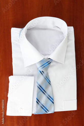 Photo: New white man's shirt with color tie on wooden background New white man's shirt with color tie on wooden background