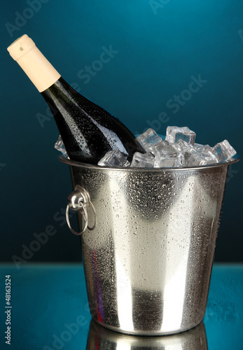 Photo: Bottle of wine in ice bucket on darck blue background Bottle of wine in ice bucket on darck blue background