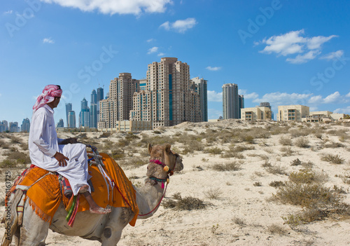 Photo: Bedouin on a camel in the desert and a modern city on the horizo Bedouin on a camel in the desert and a modern city on the horizo