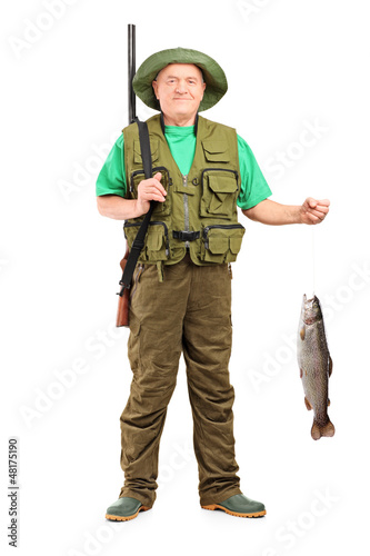 Photo: Full length portrait of a male hunter with rifle holding a fish Full length portrait of a male hunter with rifle holding a fish