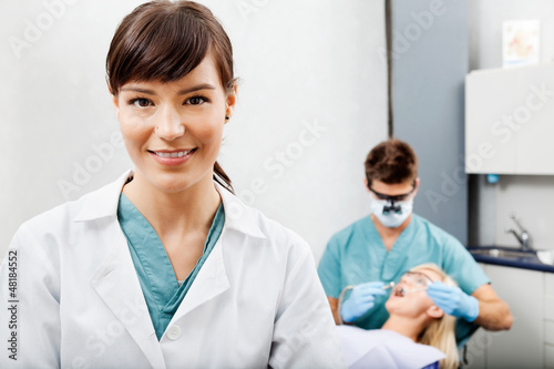 Photo: Female Assistant With Dentist Working In The Background Female Assistant With Dentist Working In The Background