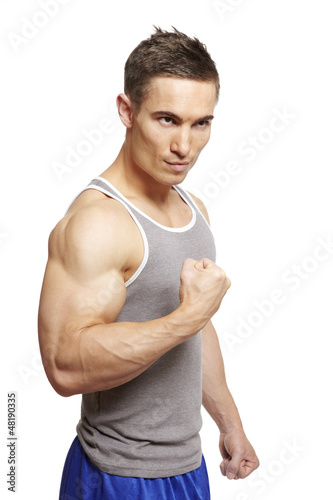 Photo: Muscular young man flexing arm muscles in sports outfit Muscular young man flexing arm muscles in sports outfit