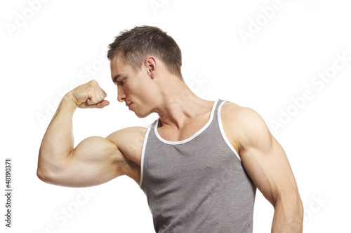 Photo: Muscular young man flexing arm muscles in sports outfit Muscular young man flexing arm muscles in sports outfit