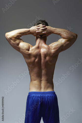 Photo: Muscular young man flexing arm muscles in sports outfit Muscular young man flexing arm muscles in sports outfit