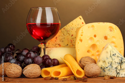 Photo: Various types of cheese on wooden table on brown background Various types of cheese on wooden table on brown background