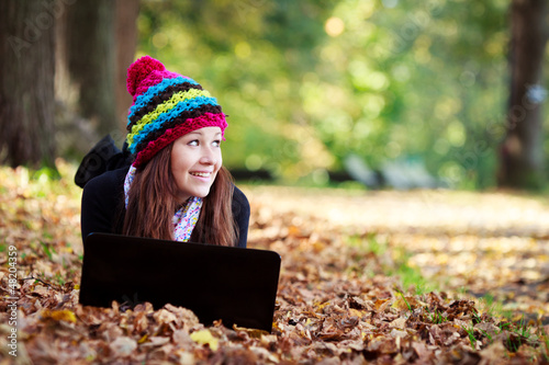 Photo: Beautiful teenage girl working on laptop in park during autumn Beautiful teenage girl working on laptop in park during autumn