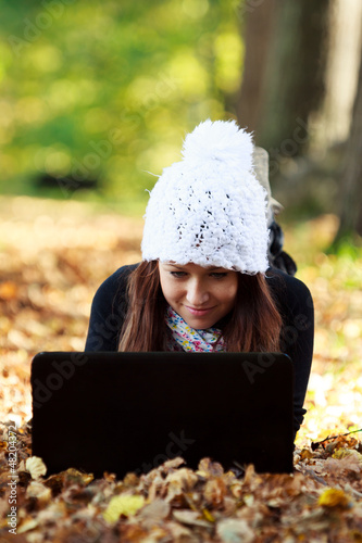 Photo: Beautiful young girl with laptop in autumn park. Young European Beautiful young girl with laptop in autumn park. Young European