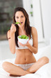 healthy young woman eating green salad on bed