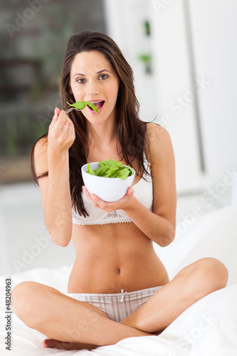 Photo: healthy young woman eating green salad on bed healthy young woman eating green salad on bed