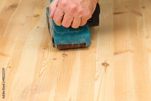 Photo: Mans hand on belt sander on pine wood Mans hand on belt sander on pine wood