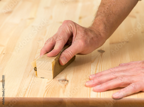 Photo: Mans hand on sanding block on pine wood Mans hand on sanding block on pine wood