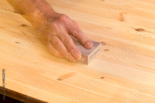 Photo: Mans hand on sanding block on pine wood Mans hand on sanding block on pine wood